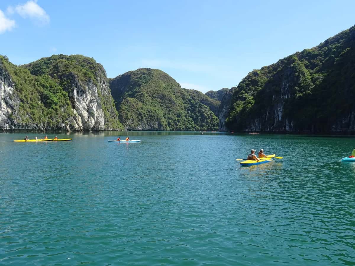 Kayakistes sur l'eau verte entre des pitons calcaires, baie d'Halong