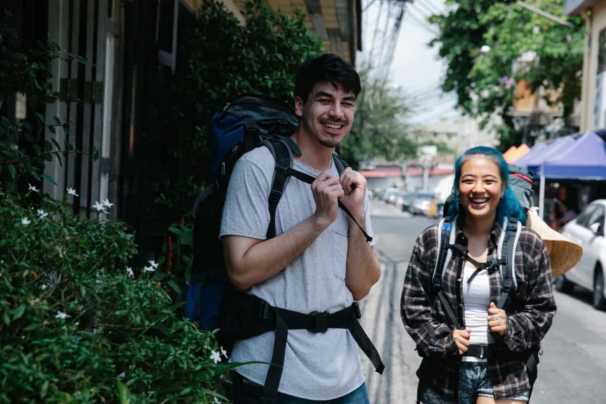 Deux voyageurs souriants avec leurs sacs à dos dans une rue ensoleillée