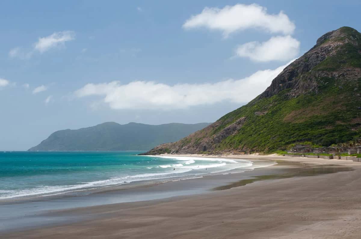 Plage de sable foncé au pied d'une colline verte, sur la côte sud de Côn Đảo
