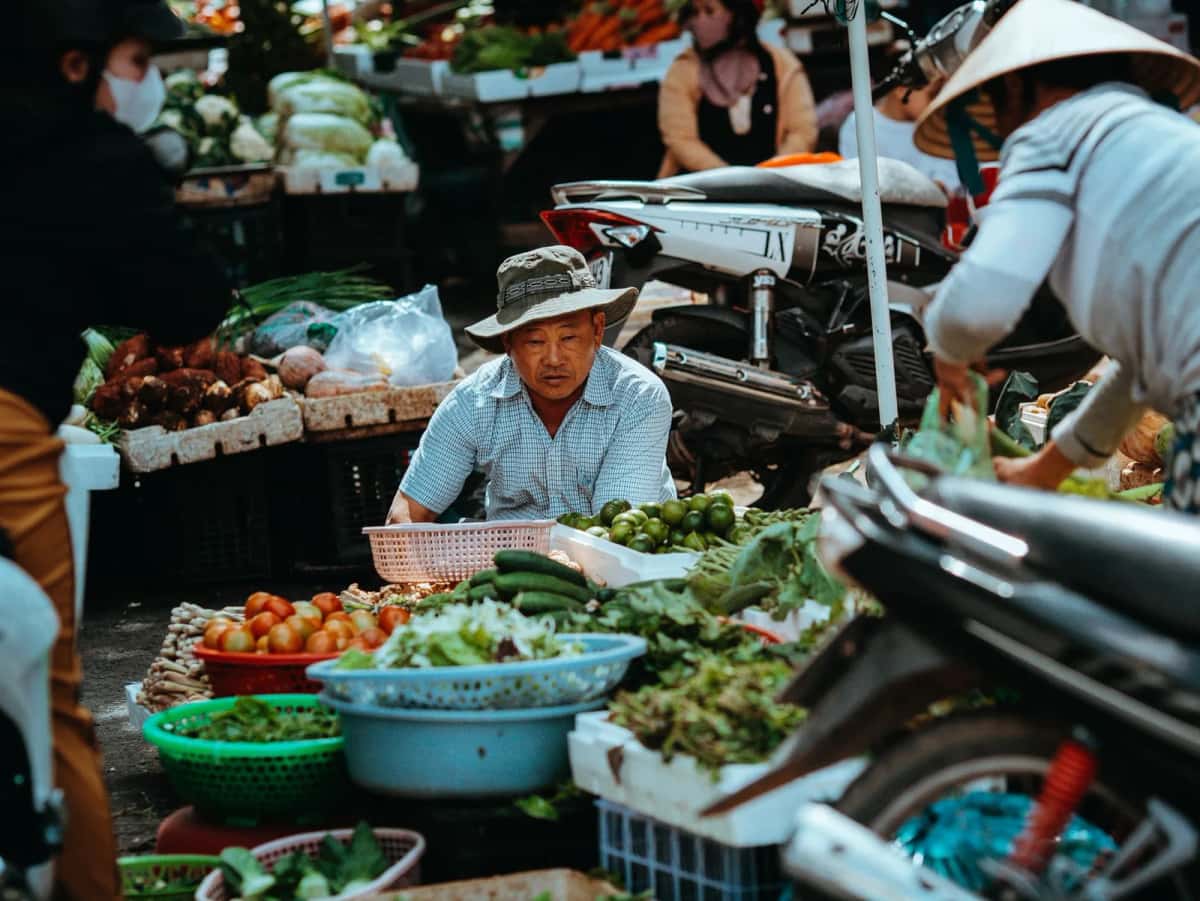 Vendeur et étals de légumes frais sur un marché local vietnamien