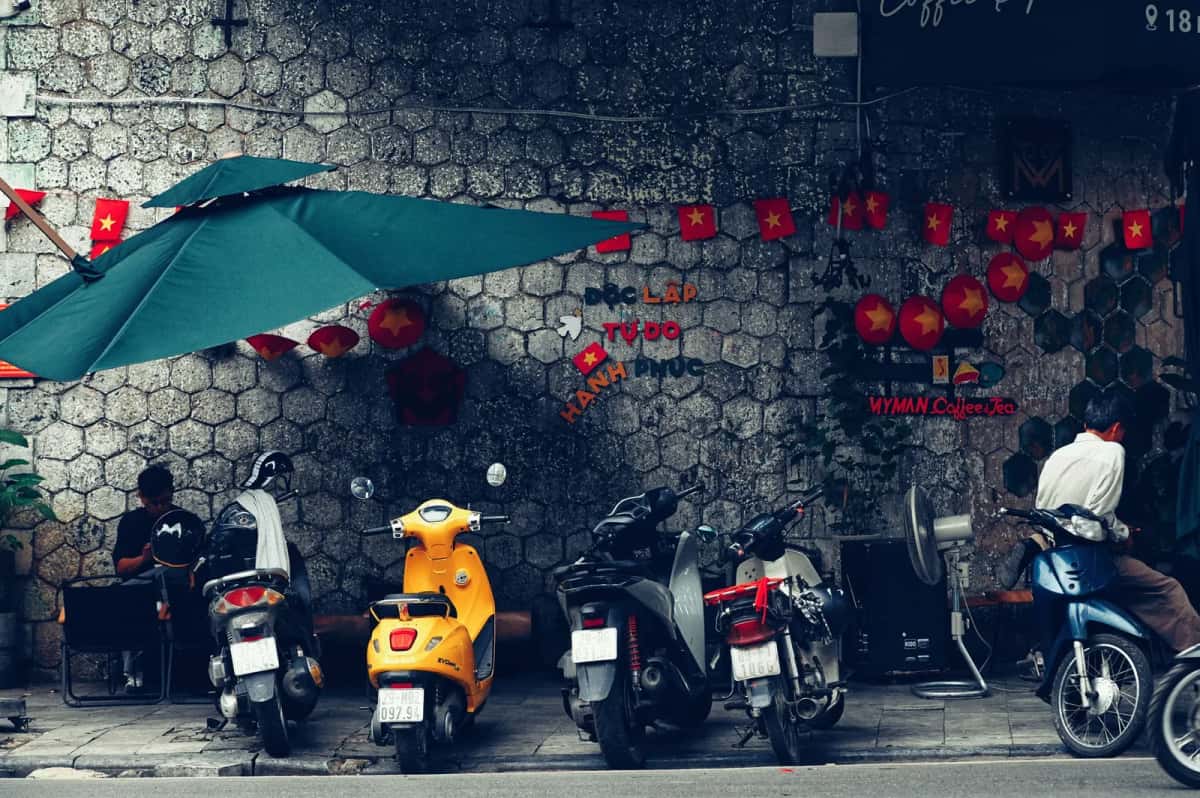Scooters garés devant un café de rue, sous un parasol et des drapeaux vietnamiens