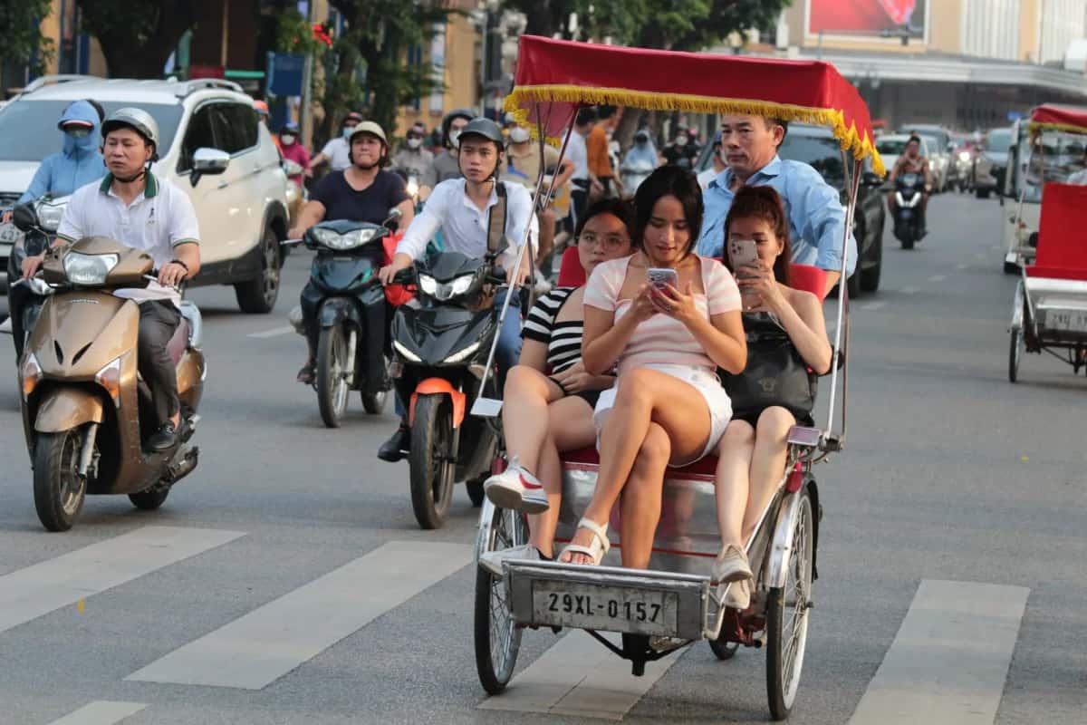 Touristes en cyclo-pousse consultant leur smartphone dans une rue animée de Hanoï, au milieu des scooters