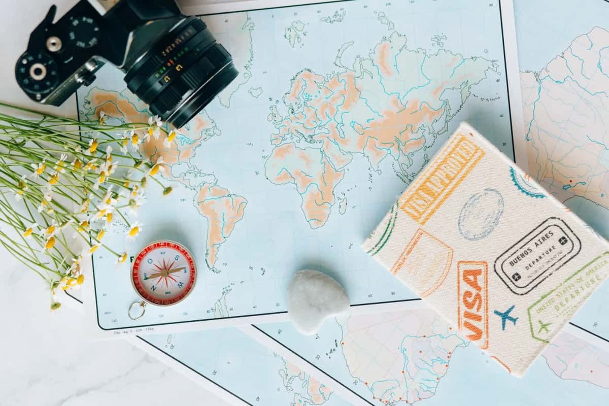 Carnet de voyage orné de tampons de visa et de départ posé sur des cartes du monde, avec un appareil photo et une boussole