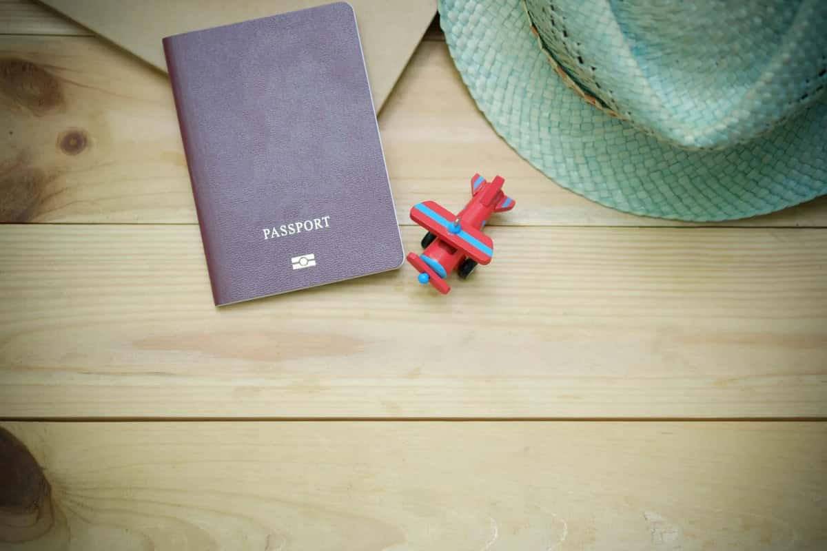 Passeport posé sur une table en bois à côté d'un petit avion jouet et d'un chapeau de paille
