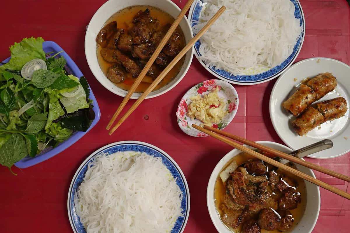 Repas de bún chả à Hanoï : boulettes et lard grillés dans leur bouillon, vermicelles de riz, herbes fraîches, ail et nem