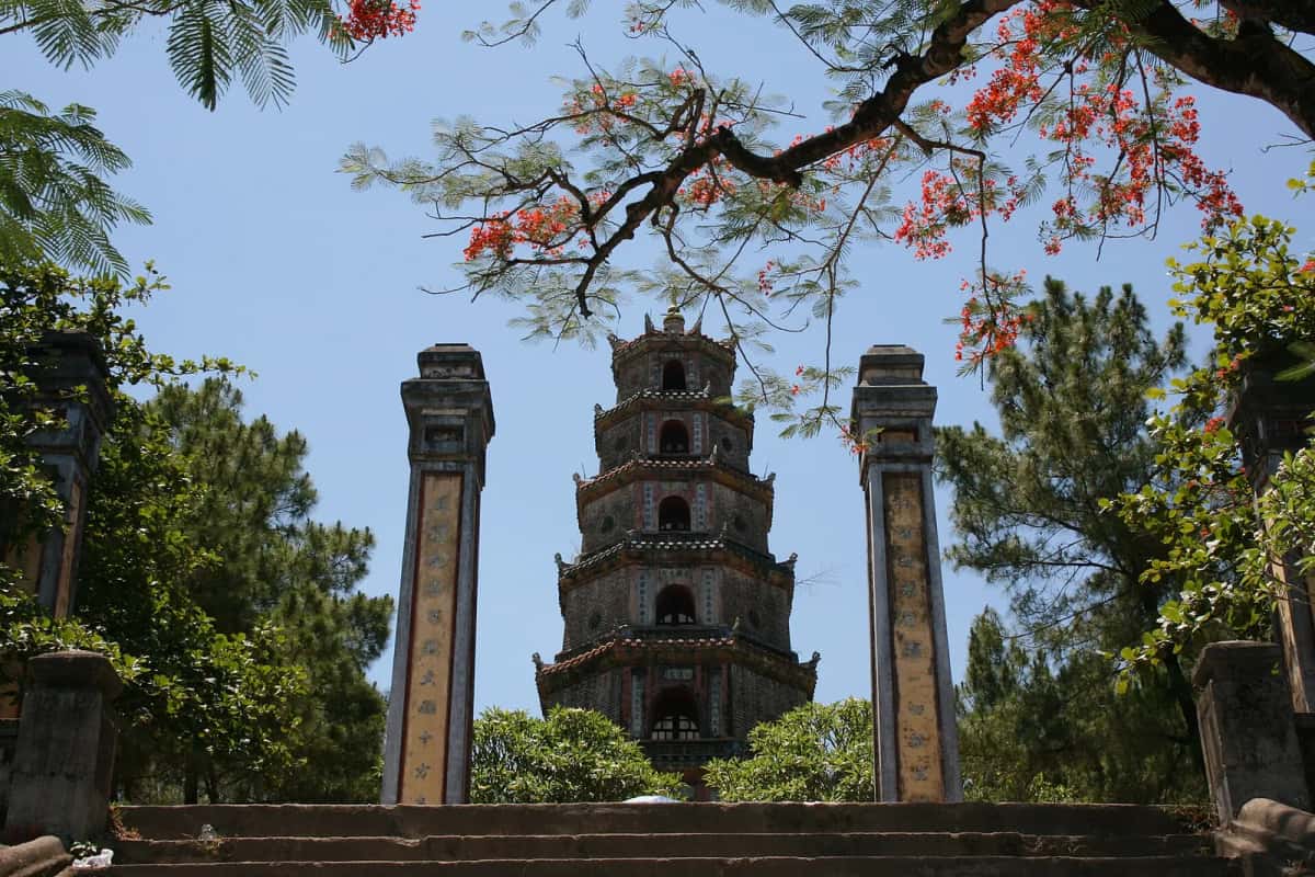 Tour de la pagode Thiên Mụ entre deux stèles, sous un flamboyant en fleurs, Huế