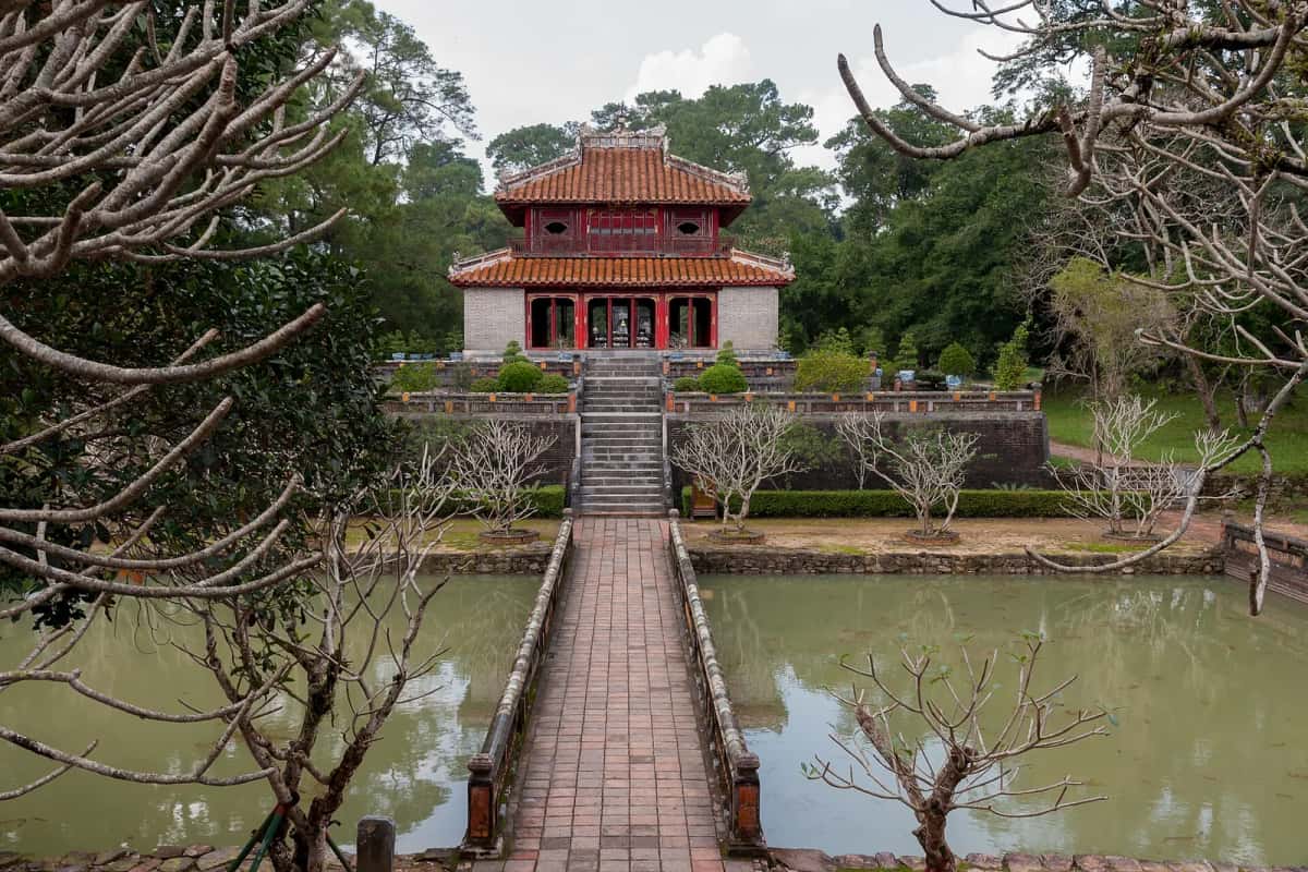 Pavillon aux toits de tuiles et passerelle de brique sur le plan d'eau du tombeau de Minh Mạng, Huế