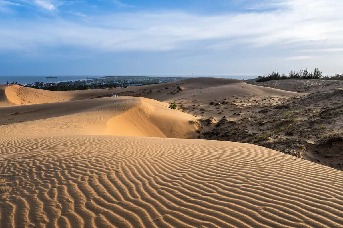 Dunes de sable rouge-orangé de Mũi Né au coucher du soleil, avec la mer et la ville de Phan Thiết au loin