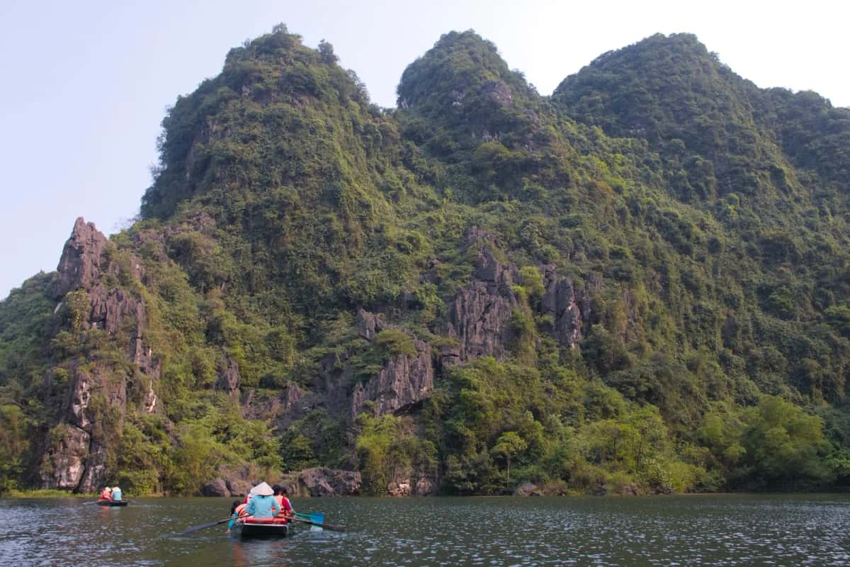 Pitons calcaires boisés au-dessus de la rivière de Tràng An, avec des barques de visiteurs, à Ninh Binh