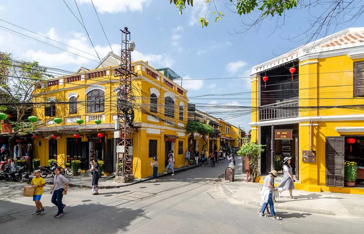 Maisons jaunes à balcons de bois et lanternes dans une rue de la vieille ville de Hội An, sous un ciel bleu