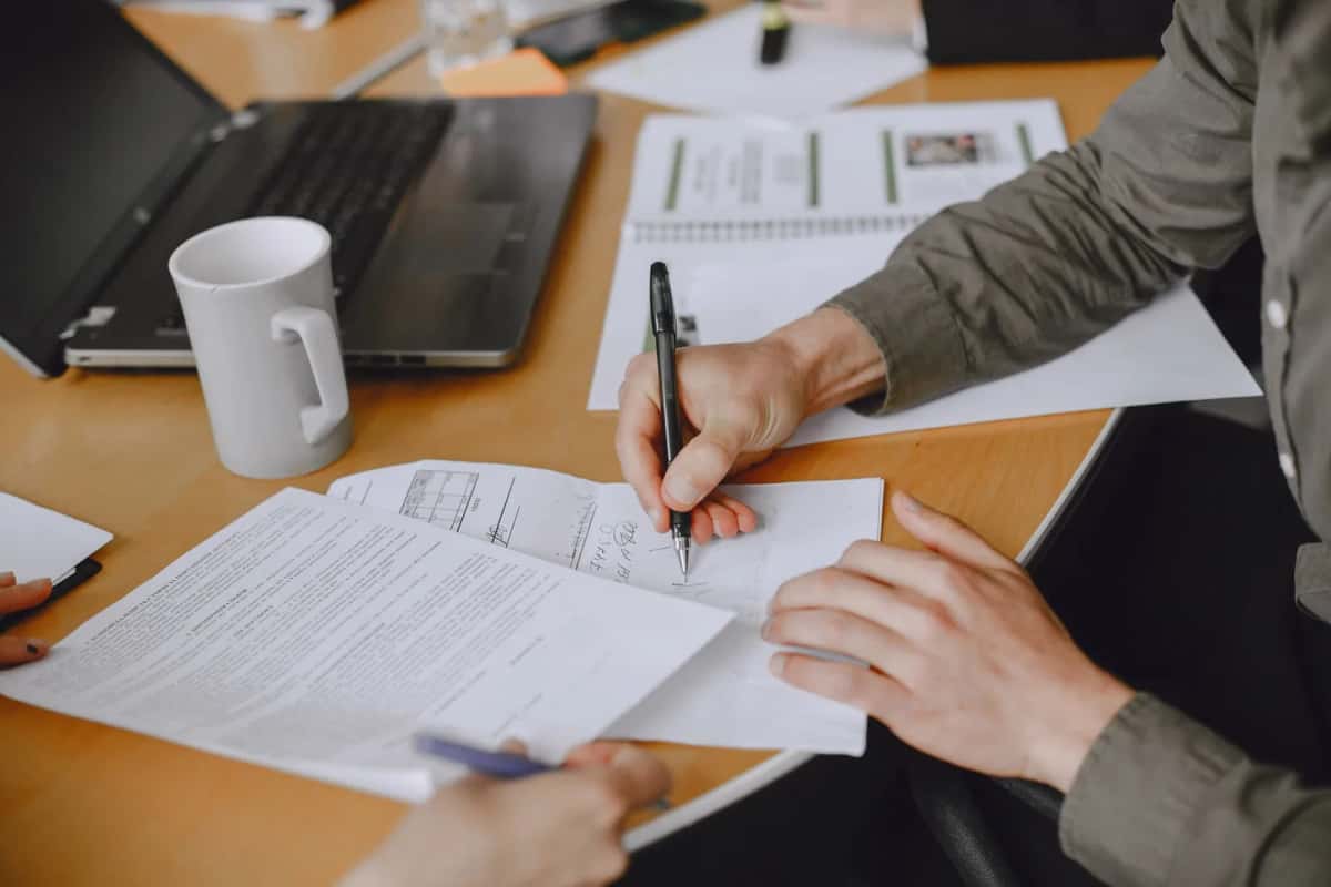 Mains signant des documents administratifs sur un bureau, à côté d'un ordinateur portable