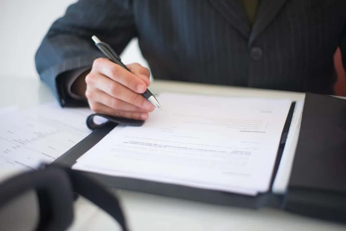 Une personne en costume remplit un dossier papier dans une chemise à un bureau
