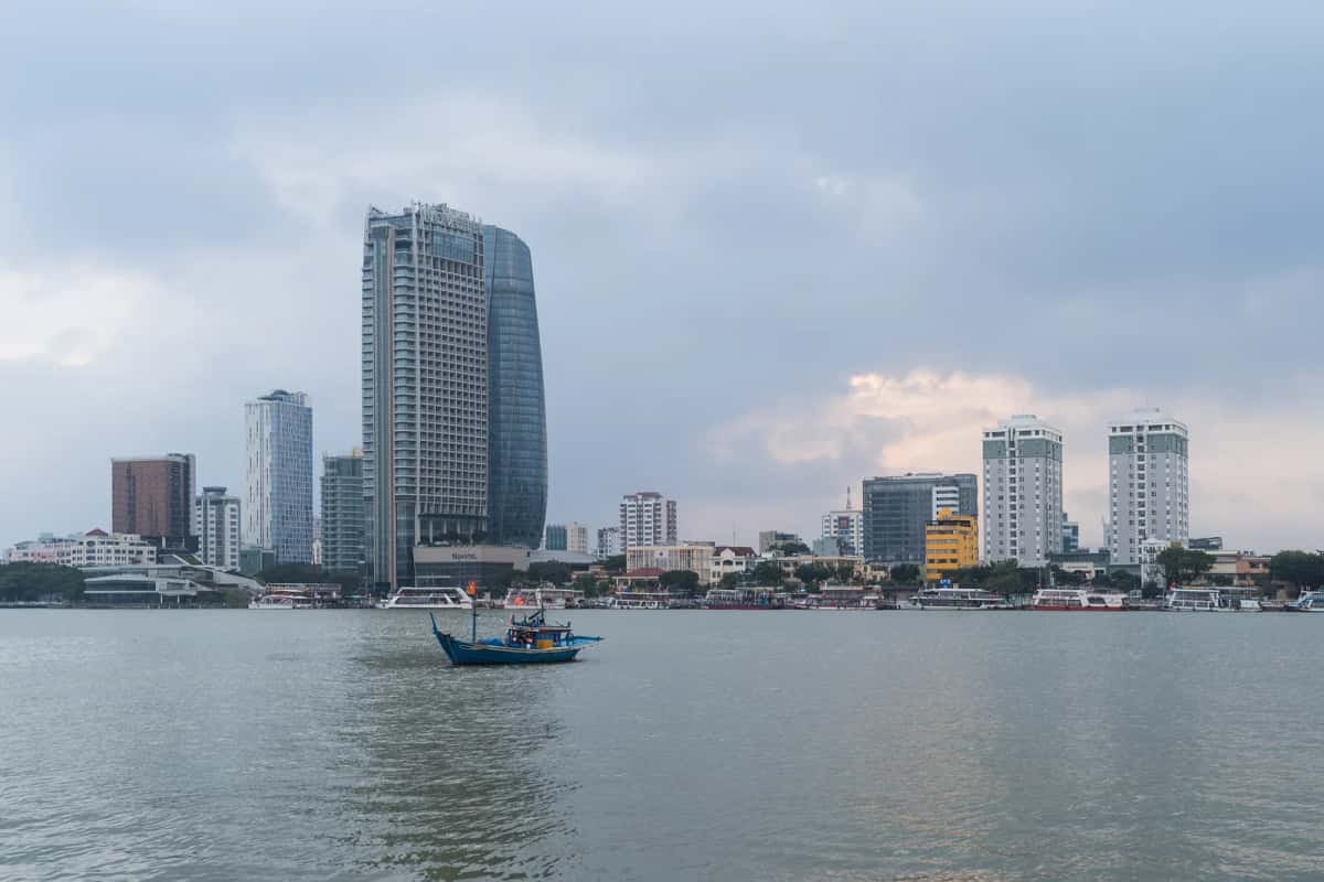Tours et immeubles de la rive du fleuve Han à Da Nang, avec une barque de pêche bleue au premier plan