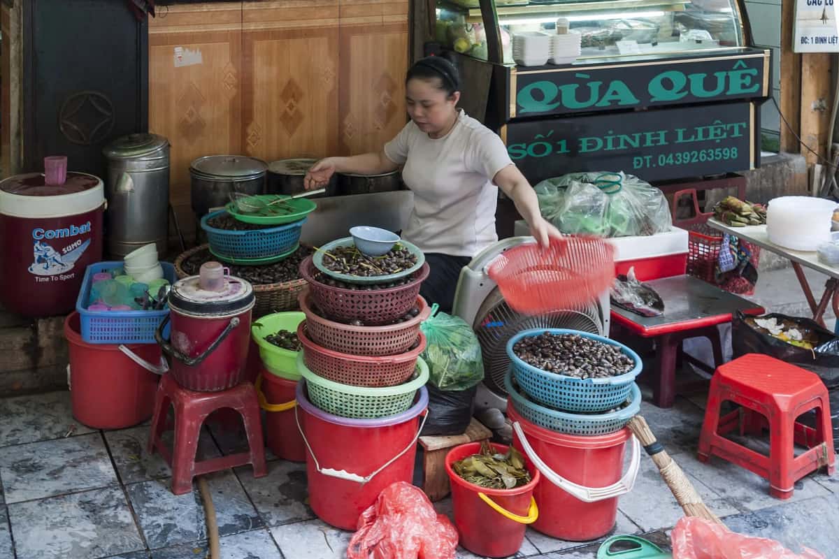 Vendeuse d'escargots devant son étal sur le trottoir de la rue Đinh Liệt, vieux quartier de Hanoï